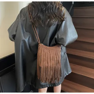 Sac bandoulière en daim marron avec franges porté par un mannequin sur un escalier