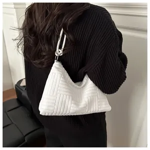 Detail shot of a white tote bag with embossed checkered texture on black knitwear