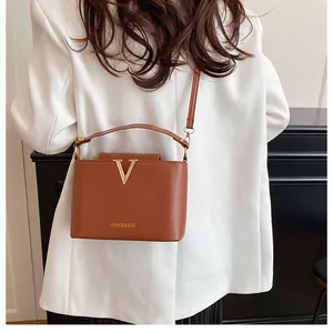 Detail of brown leather handbag with gold V-decoration and thin shoulder strap