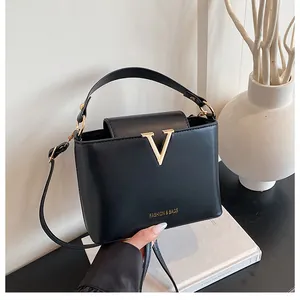 Detail of black matte leather handbag featuring gold V-metal buckle on white book