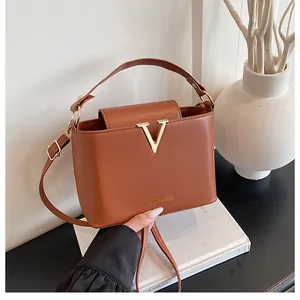 Detail of a brown leather bucket bag with a golden V-shaped metal logo on a black table