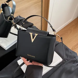 Minimalist black bucket bag with golden V-shaped hardware and detachable shoulder strap