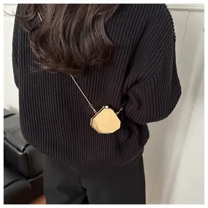 Détail d'un mini sac à chaîne doré hexagonal porté sur une tenue en tricot noir