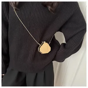 Détail d'un mini sac géométrique doré avec fine chaîne sur un pull en tricot noir
