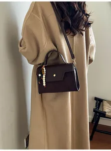 Detail of dark brown leather baguette bag with bead charm worn over a camel coat