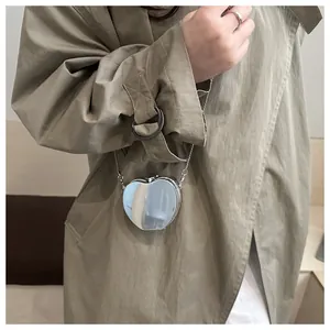 Gros plan d'un mini sac cœur argenté porté avec un trench-coat beige élégant et moderne
