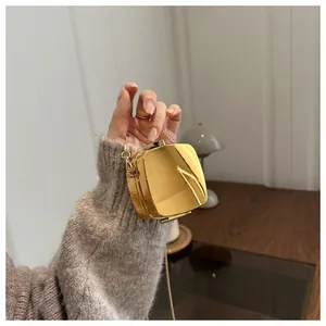 Gros plan d'un mini sac boîte en métal doré poli avec bandoulière chaîne à la main