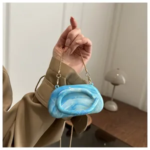 Detail of blue marble acrylic clutch with gold chain strap and curved top handle