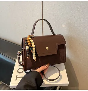 Detail van de donkerbruine leren baguette-tas met boho-parelkwast en gouden knoopdetail