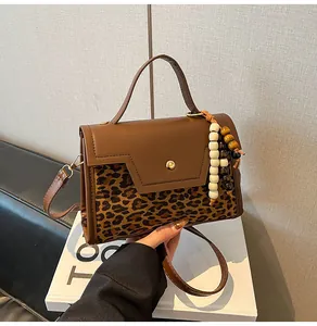 Close-up of brown leopard print baguette bag with golden buckle and wooden bead charm