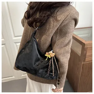 Detail of a black hobo bag in faux patent leather with a cute bear charm and tassel