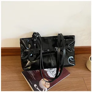 Vue détaillée du sac à bandoulière noir brillant avec œillets métalliques et boucles