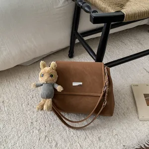 Brown suede shoulder bag with chain strap and cute rabbit charm on white bedding