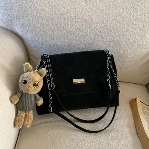 Chic black matte shoulder bag with silver chain strap and plush rabbit charm on a beige sofa