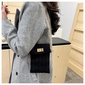 Close-up of black quilted velvet crossbody bag with golden chain strap on a grey coat