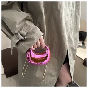 Détail du sac demi-lune rose métallisé avec chaîne dorée sur un trench-coat vert