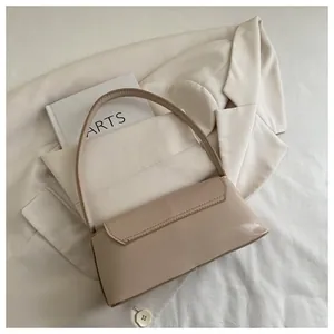 Glossy beige baguette bag with flap closure placed on a light blazer and arts book