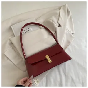 Detail view of burgundy patent leather handbag with golden lock on a white suit
