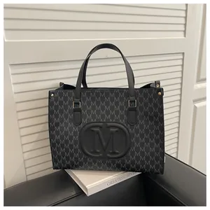 Detailed view of the black M-letter pattern on a dark grey leather tote bag on a sofa