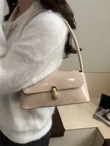 Glossy cream shoulder bag with gold clasp shown on model in a modern office setting