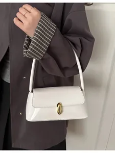 White glossy patent leather underarm bag with gold metal clasp on a stylish wool coat