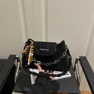 Sac bandoulière noir mat chic avec perles en bois et chaîne florale sur chaise