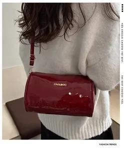 Detalle de bolso cilíndrico de charol rojo oscuro con logo dorado y cremallera