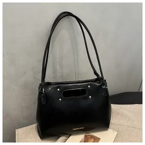 Detail of black faux leather bag with oval cutout handle and gold decorative rivets