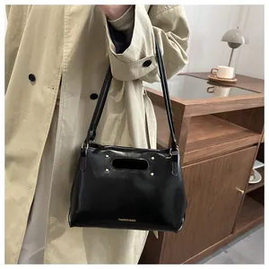 Detail of black glossy leather handbag with gold rivets and oval cutout handle on shoulder