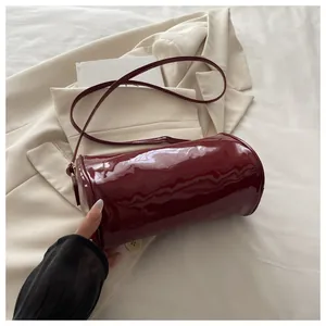 Gros plan sur le sac cylindre en cuir verni bordeaux brillant avec bandoulière