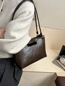 Brown leather tote bag with oval cutout handle and gold rivets for business commute