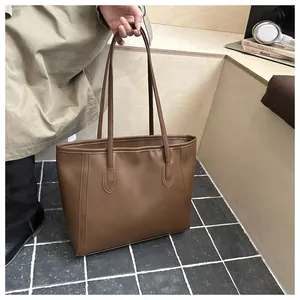 Detailed view of deep brown leather tote bag with slim shoulder straps on wooden background