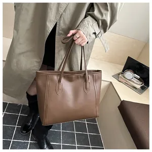 Brown leather tote bag being held by a model in a stylish office or daily commute setting