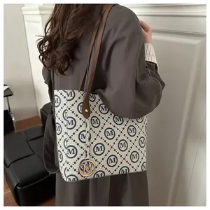 Detalle de un bolso tote grande beige con estampado de monogramas y asas de cuero