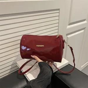 Glanzende wijnrode cilindrische tas met goudkleurig logo en lange schouderband