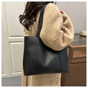 Klassische schwarze Leder-Einkaufstasche zum beigen Mantel für einen stilvollen Büro-Look