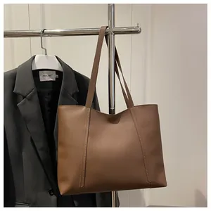 Detail einer braunen Leder-Tote-Bag mit vertikalen Nähten vor minimalistischem Anzughintergrund