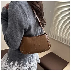 Détail d'un sac à bandoulière marron motif crocodile avec patch cœur et rivets argentés