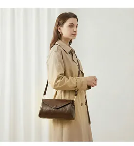 Detail van een donkerbruine oliewas lederen enveloptas gedragen met een elegante beige trenchcoat