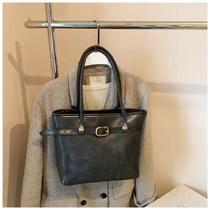 Detail einer dunkelmatten Leder-Tote-Bag mit dekorativem Riemen und goldener Schnalle