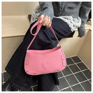 Sac à bandoulière rose avec texture crocodile et détail de cœur porté par un mannequin