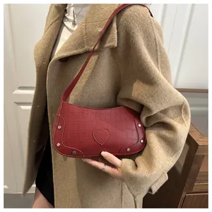 Détail du sac baguette rouge embossé croco avec patch cœur porté sur un manteau en laine