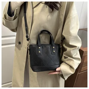 Detail of black quilted bucket bag with gold rivets on model wearing a khaki coat