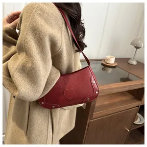 Détail du sac bandoulière rouge foncé en cuir crocodile avec patch cœur et rivets en métal