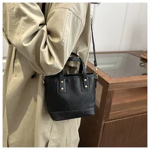 Detail of black quilted bucket bag with gold rivets and leather strap on khaki coat