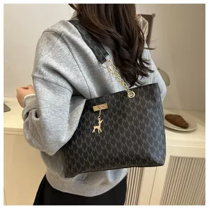 Detail of grey tote bag with M-pattern print, chain strap and gold deer charm on model