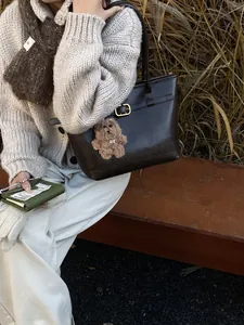 Große dunkelbraune Leder-Tote-Bag mit Bärenanhänger in herbstlicher Outdoor-Szene