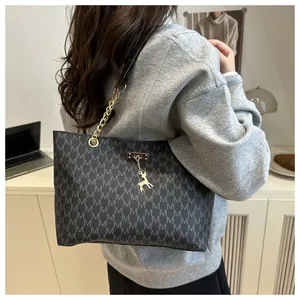 Detail of black tote bag featuring grey M patterns, gold chain handles, and deer charm