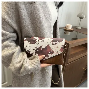Dettaglio della borsa a busta in pelle marrone e stampa mucca con catena dorata elegante
