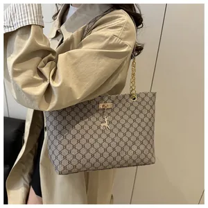 Detail of a brown monogram tote bag with gold chain strap and deer charm on a trench coat
